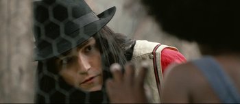 Movie still from “Mister Lonely” (2007), directed by Harmony Korine – A man with long black hair wearing a black hat; Close Up shot, Over the shoulder angle