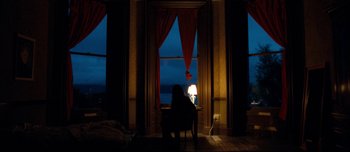 Movie still from “Mister Lonely” (2007), directed by Harmony Korine – A woman sitting in a chair in front of a window at night; Extreme Wide shot, Low angle