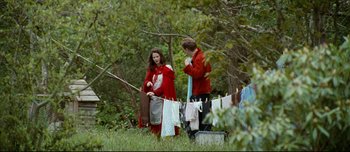 Movie still from “Mister Lonely” (2007), directed by Harmony Korine – A woman and a man in a red coat hanging clothes on a clothesline in a wooded area; Wide shot, Over the shoulder angle