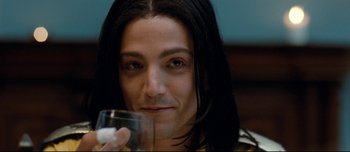 Movie still from “Mister Lonely” (2007), directed by Harmony Korine – A man with long black hair is holding a glass of water; Close Up shot, Low angle