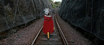 Movie still from “Mister Lonely” (2007), directed by Harmony Korine – A person with an umbrella walking down a train track; Wide shot, Overhead angle