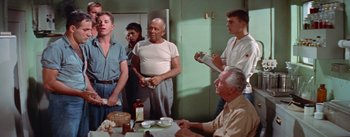 Movie still from “Mister Roberts” (1955), directed by John Ford – A group of men standing around a table; Medium shot, Low angle