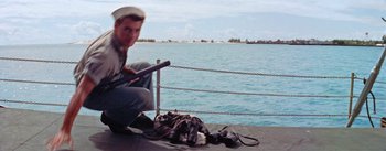 Movie still from “Mister Roberts” (1955), directed by John Ford – A man sitting on a pier next to a body of water; Medium shot, High angle