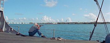 Movie still from “Mister Roberts” (1955), directed by John Ford – A man sitting on a pier looking at the water; Wide shot, High angle