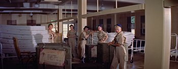 Movie still from “Mister Roberts” (1955), directed by John Ford – A group of women standing next to each other in a warehouse; Wide shot, Low angle