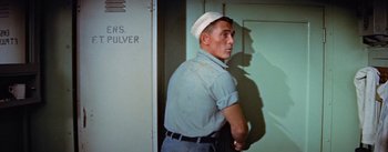 Movie still from “Mister Roberts” (1955), directed by John Ford – A man wearing a sailor's hat standing next to a door; Medium shot, Low angle