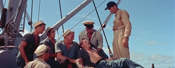 Movie still from “Mister Roberts” (1955), directed by John Ford – A group of men standing around a man on a boat; Medium shot, Overhead angle