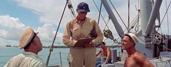 Movie still from “Mister Roberts” (1955), directed by John Ford – An old man in a cap is on a boat looking at a clipboard; Medium shot, Low angle