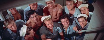 Movie still from “Mister Roberts” (1955), directed by John Ford – A group of men sitting next to each other on the ground; Medium shot, High angle