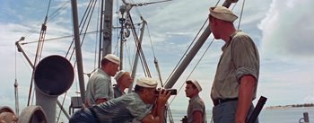 Movie still from “Mister Roberts” (1955), directed by John Ford – A group of men on a boat taking pictures; Medium shot, High angle