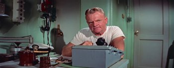 Movie still from “Mister Roberts” (1955), directed by John Ford – A man sitting at a table looking at something in a box; Close Up shot, Low angle