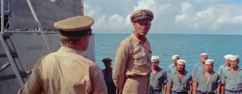 Movie still from “Mister Roberts” (1955), directed by John Ford – A man in a uniform standing next to a boat; Medium shot, Over the shoulder angle