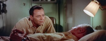 Movie still from “Mister Roberts” (1955), directed by John Ford – A man sitting at a table with his hand on his chest; Close Up shot, High angle