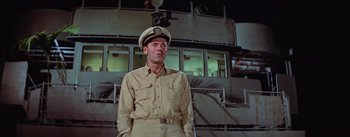 Movie still from “Mister Roberts” (1955), directed by John Ford – A man in a uniform standing in front of a boat; Medium shot, Low angle