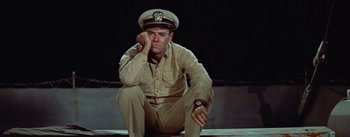 Movie still from “Mister Roberts” (1955), directed by John Ford – A man in a military uniform sitting on the ground; Medium shot, High angle