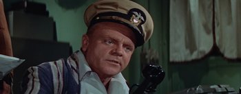 Movie still from “Mister Roberts” (1955), directed by John Ford – An older man wearing a hat and holding a phone to his ear; Close Up shot, High angle