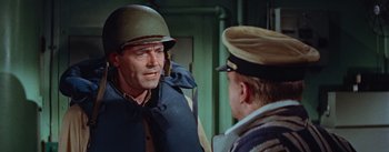 Movie still from “Mister Roberts” (1955), directed by John Ford – A man wearing a hat and a vest talking to another man; Medium shot, Over the shoulder angle