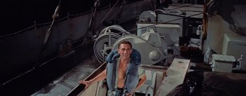 Movie still from “Mister Roberts” (1955), directed by John Ford – A man in a blue vest standing next to a boat; Medium shot, High angle