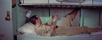 Movie still from “Mister Roberts” (1955), directed by John Ford – A man laying in a bed with a book; Medium shot, Overhead angle