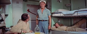 Movie still from “Mister Roberts” (1955), directed by John Ford – A man standing in front of two other men in a room; Medium shot, Low angle