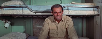 Movie still from “Mister Roberts” (1955), directed by John Ford – A man sitting in front of a bed in a room; Medium shot, High angle