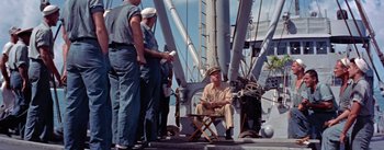 Movie still from “Mister Roberts” (1955), directed by John Ford – A man sitting on a deck of a boat; Wide shot, High angle