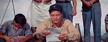 Movie still from “Mister Roberts” (1955), directed by John Ford – A man sitting on the ground looking down at a piece of paper; Close Up shot, High angle