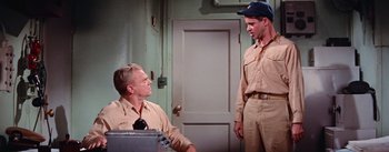 Movie still from “Mister Roberts” (1955), directed by John Ford – Two men in tan work clothes talking to each other; Medium shot, Over the shoulder angle