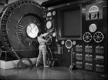 Movie still from “Modern Times” (1936), directed by Charles Chaplin – A man is standing in front of a large machine; Wide shot, Low angle