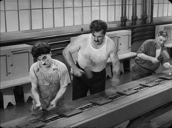 Movie still from “Modern Times” (1936), directed by Charles Chaplin – A man and a boy working in a factory; Medium shot, High angle
