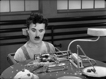 Movie still from “Modern Times” (1936), directed by Charles Chaplin – A man with a mustache sitting in front of a machine; Medium shot, High angle