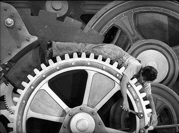 Movie still from “Modern Times” (1936), directed by Charles Chaplin – A man working on a large gear in a machine shop; Wide shot, High angle