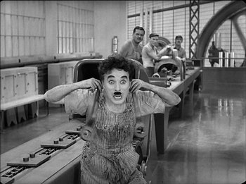 Movie still from “Modern Times” (1936), directed by Charles Chaplin – An old black and white photo of a man in a factory; Medium shot, Low angle