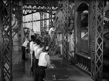Movie still from “Modern Times” (1936), directed by Charles Chaplin – A black and white photo of men working in an industrial setting; Wide shot, High angle