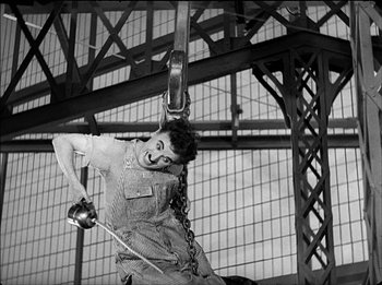 Movie still from “Modern Times” (1936), directed by Charles Chaplin – A man hanging from a metal ring with chains; Medium shot, Low angle