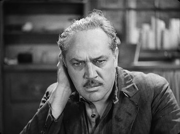 Movie still from “Modern Times” (1936), directed by Charles Chaplin – An older man is holding his hand up to his ear; Close Up shot, High angle