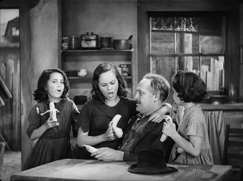 Movie still from “Modern Times” (1936), directed by Charles Chaplin – An old photo of a man and two young girls; Medium shot, High angle