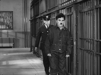 Movie still from “Modern Times” (1936), directed by Charles Chaplin – A man walking next to another man in a uniform; Wide shot, High angle