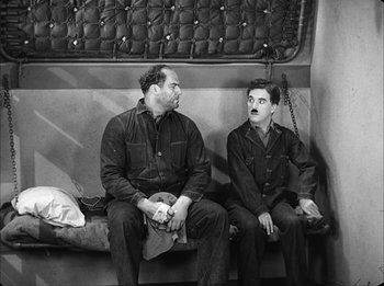 Movie still from “Modern Times” (1936), directed by Charles Chaplin – Two men sitting on a bench in front of each other; Wide shot, High angle