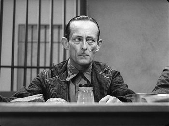 Movie still from “Modern Times” (1936), directed by Charles Chaplin – A black and white photo of a man sitting at a table; Close Up shot, Over the shoulder angle