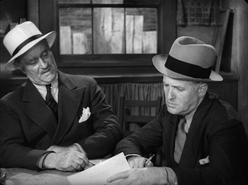 Movie still from “Modern Times” (1936), directed by Charles Chaplin – Two men sitting at a table with papers and hats on; Medium shot, Over the shoulder angle