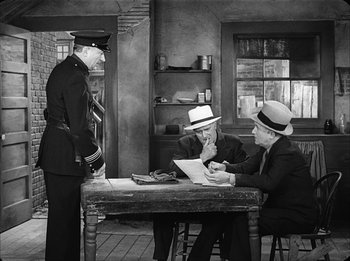 Movie still from “Modern Times” (1936), directed by Charles Chaplin – Two men are sitting at a table and one is wearing a hat; Medium shot, High angle