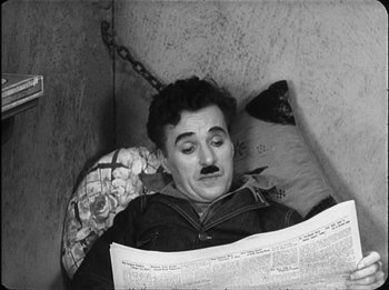 Movie still from “Modern Times” (1936), directed by Charles Chaplin – A black and white photo of a man reading a newspaper; Medium shot, High angle