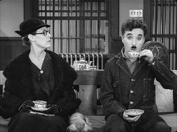 Movie still from “Modern Times” (1936), directed by Charles Chaplin – A man and a woman sitting next to each other holding bowls; Medium shot, High angle