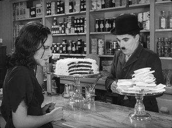 Movie still from “Modern Times” (1936), directed by Charles Chaplin – A woman sitting at a table with a man in front of a cake; Medium shot, Over the shoulder angle