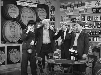 Movie still from “Modern Times” (1936), directed by Charles Chaplin – A group of men standing around a table drinking wine; Wide shot, High angle