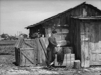 Movie still from “Modern Times” (1936), directed by Charles Chaplin – A man standing in front of a wooden building; Wide shot, Low angle