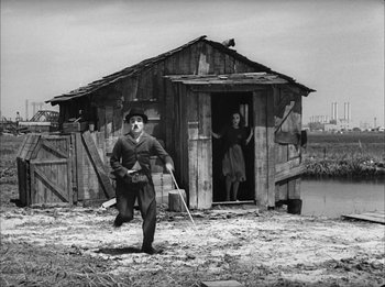 Movie still from “Modern Times” (1936), directed by Charles Chaplin – A man and a woman are standing in front of a shack; Wide shot, Low angle