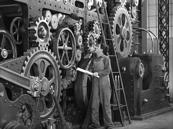 Movie still from “Modern Times” (1936), directed by Charles Chaplin – A man standing next to a large machine; Wide shot, Low angle