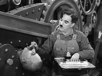 Movie still from “Modern Times” (1936), directed by Charles Chaplin – An old photo of a man working on a machine; Medium shot, High angle